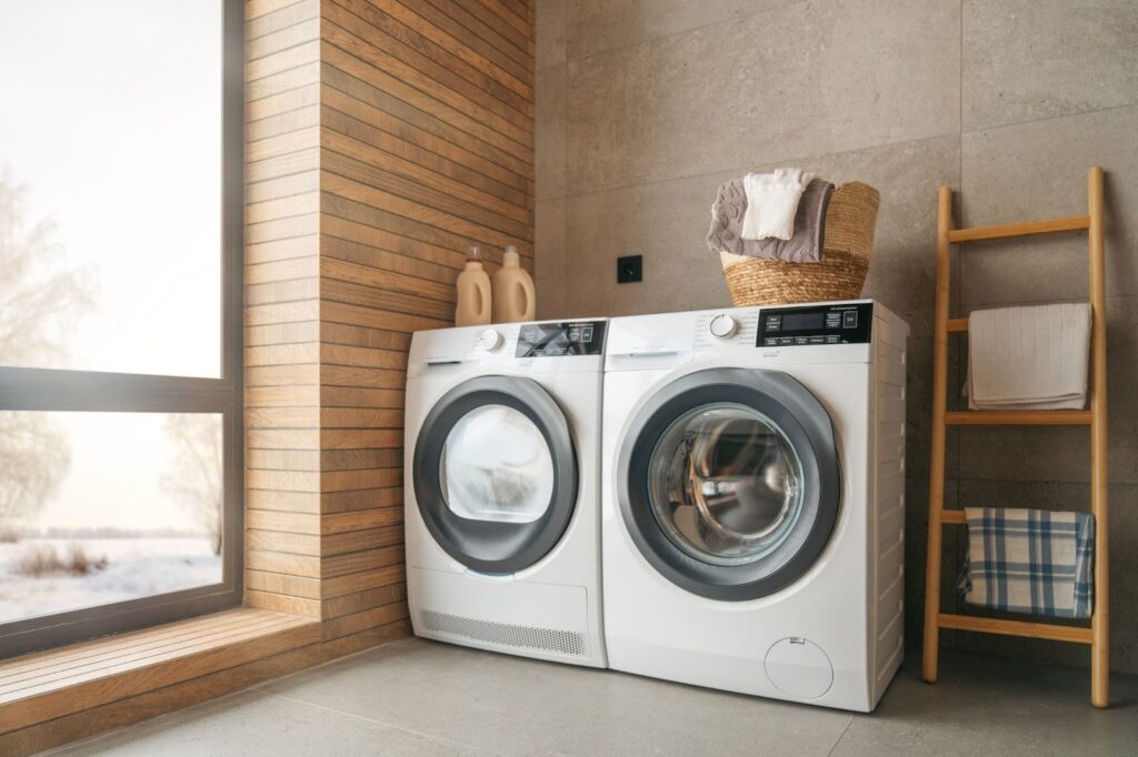 A laundry room with two white washing machines, a basket of laundry, and a wooden ladder towel rack.