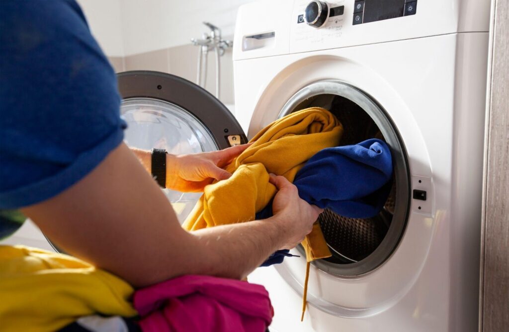 A man is inserting clothes into a washing machine ready to start washing